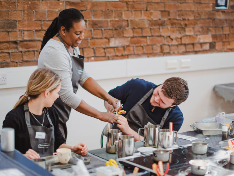 A teacher helps two students at a candle making class
